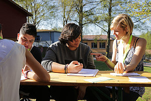 drei Jugendliche sitzen am Tisch über ihren Schulbüchern zusammen