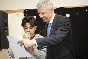 Staatssekretär Dr. Manuel Lösel schaut einem Jugendlichen über die Schulter.