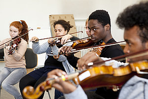 Vier Kinder mit unterschiedlichen Hautfarben sitzen im Kreis und spielen Geige.