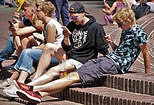 Jungen im Teenageralter sitzen draußen aus einer Treppe und schauen alle in ein eigenes Smartphone.