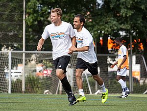 Zwei junge Männder spielen gemeinsam Fußball in Shirts des Programms Willkommen im Fußball.