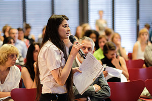 eine Teilnehmerin spricht ins Mikrofon und stellt eine Frage an die Podiumsgäste