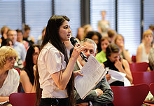 eine Teilnehmerin spricht ins Mikrofon und stellt eine Frage an die Podiumsgäste