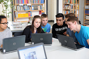 Schülerinnen und Schüler sitzen um zwei Laptops herum.