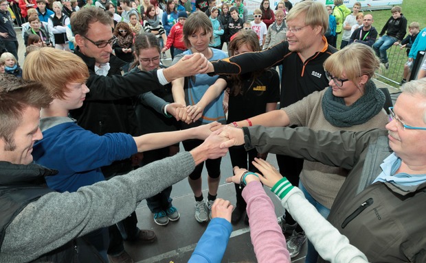 Jugendliche und Erwachsene stehen im Kreis und legen die Hände zusammen. Bildquelle: DKJS