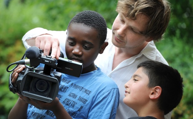 Ein Kameramann erklärt zwei Jungen die Bedienung der Kamera.