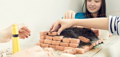Ein Mädchen baut mit kleinen Lehmziegeln eine Mauer