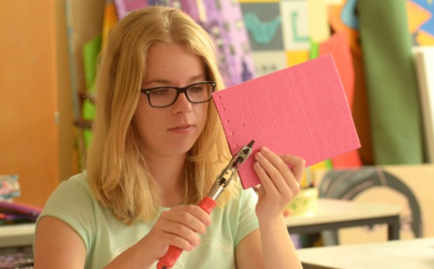 Schülerin stanzt mit einer Lochzange in eine Pappe